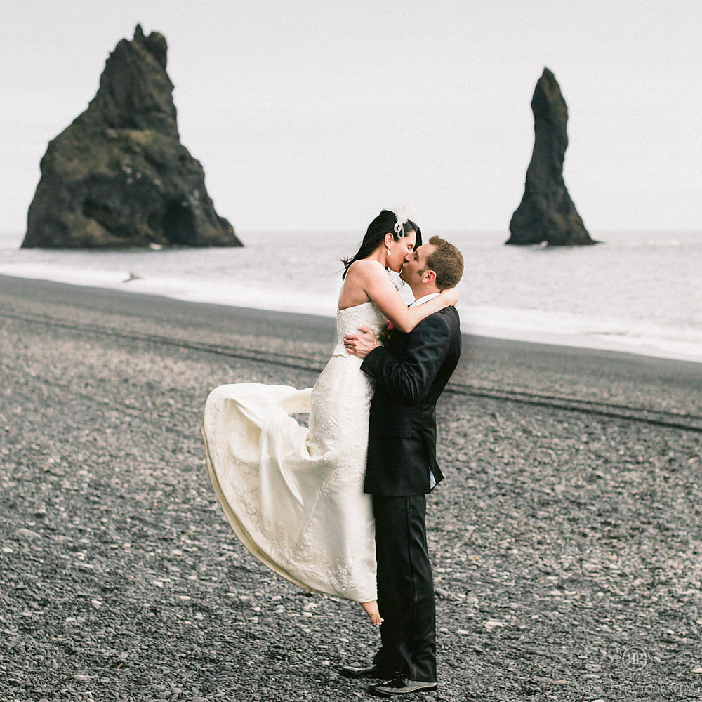 after their iceland wedding ceremony the couple kiss on the black sand beach of Vik. 